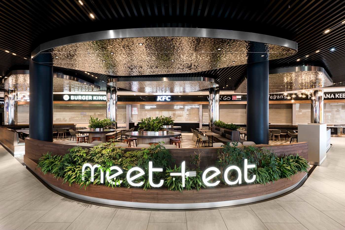 Modern food court with Burger King and KFC, featuring 'meet + eat' sign and greenery.