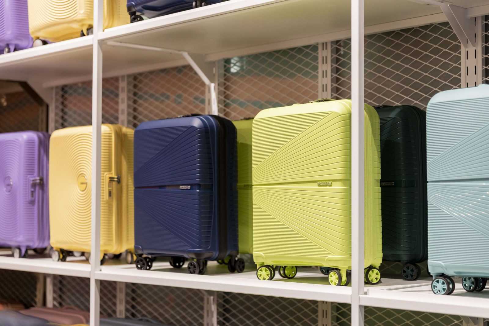 Colorful American Tourister suitcases on display shelves.