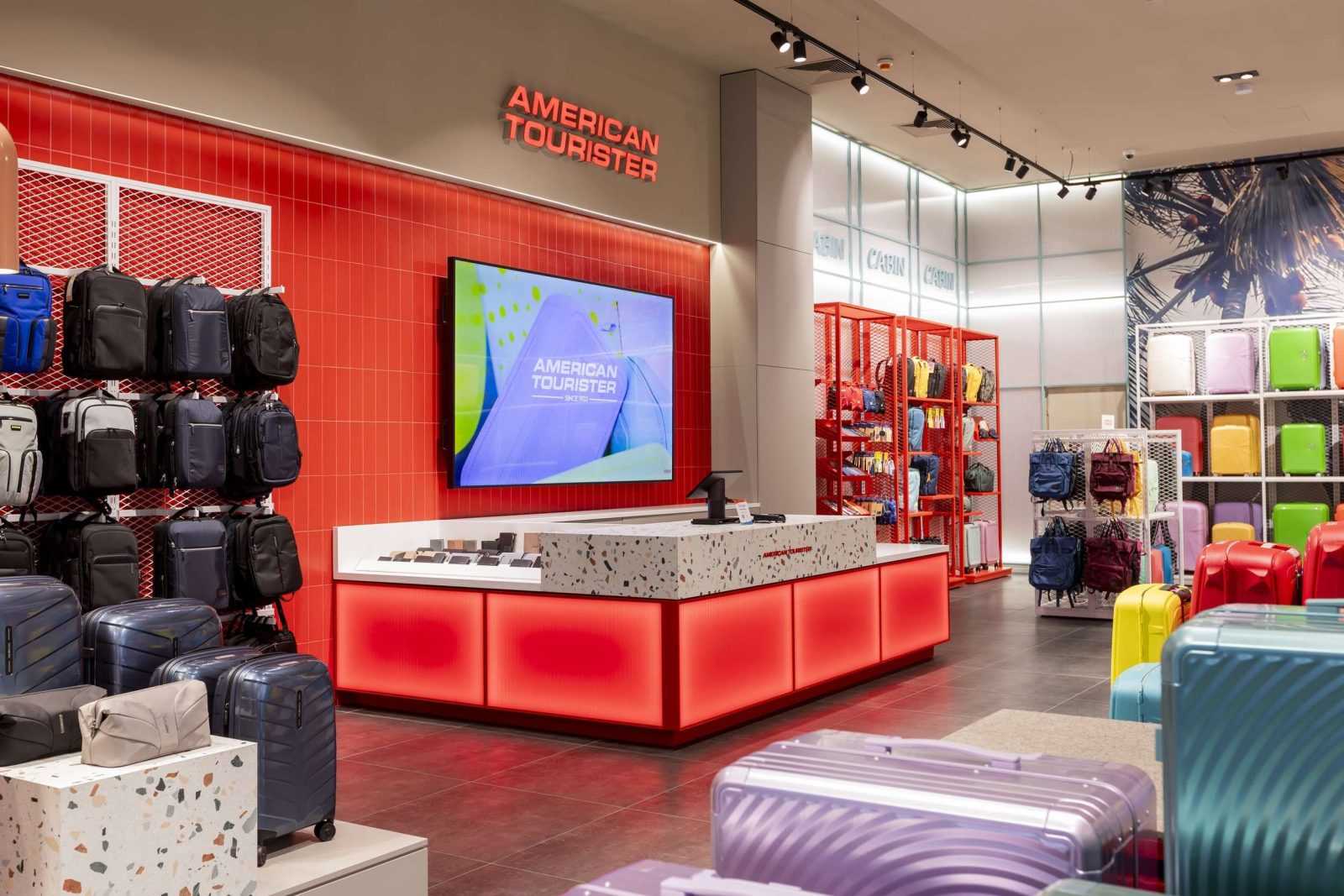 American Tourister store interior with colorful luggage and red accent walls.