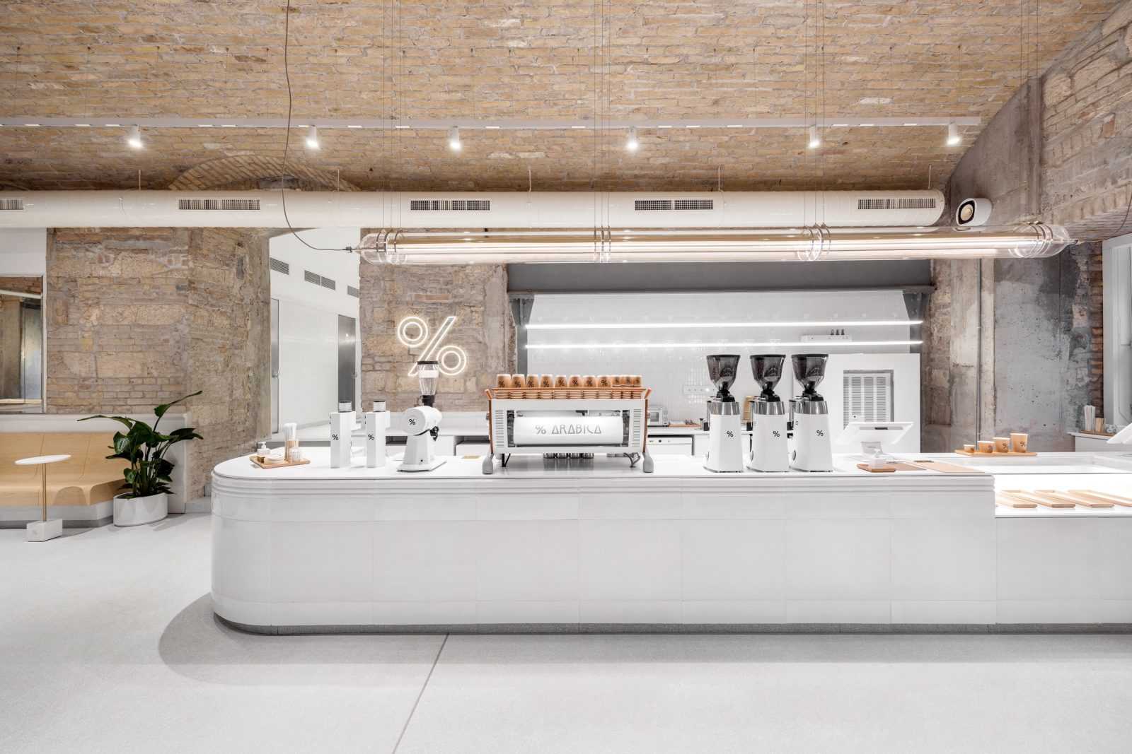 Modern minimalist coffee shop interior with exposed brick ceiling and white counter.