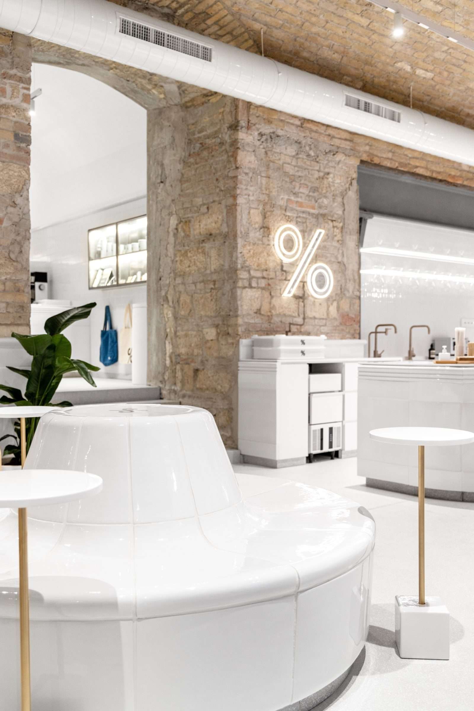 Modern minimalist coffee shop interior with white furniture and exposed brick walls.