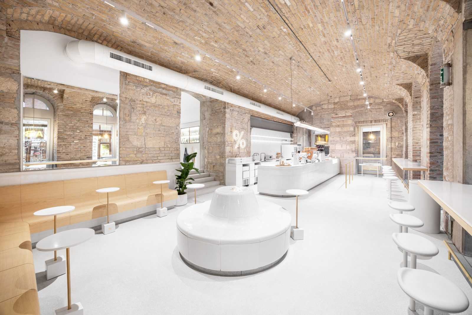Modern minimalist café interior with exposed brick ceiling and white furniture.