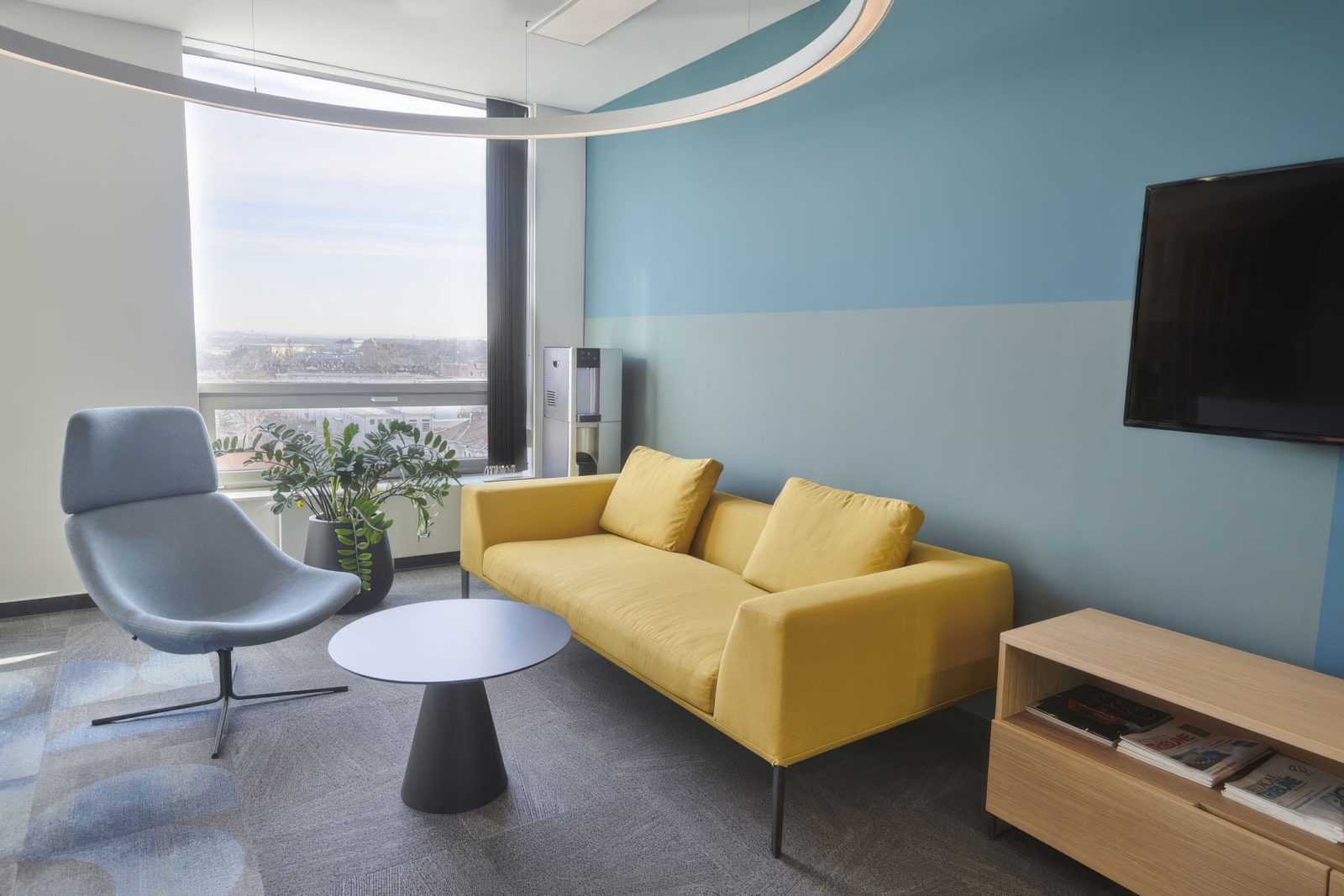 Modern office lounge with yellow sofa and city view.