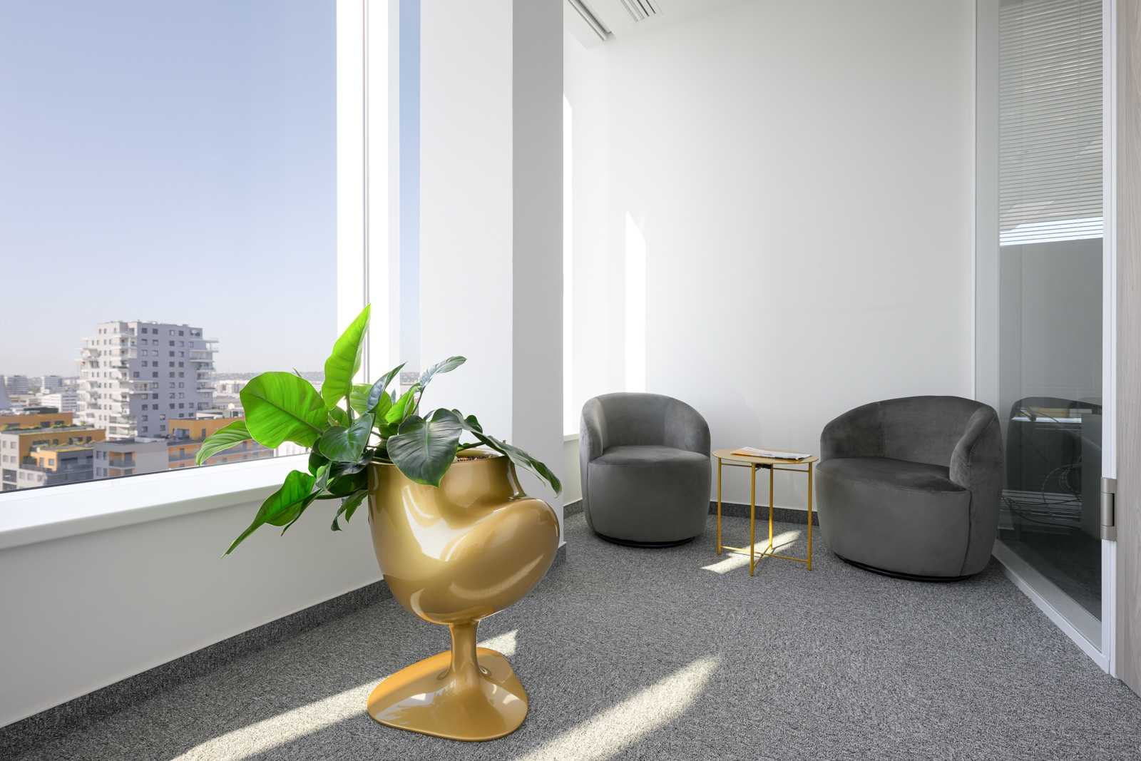 Modern office lounge with gray chairs and gold plant pot near window.