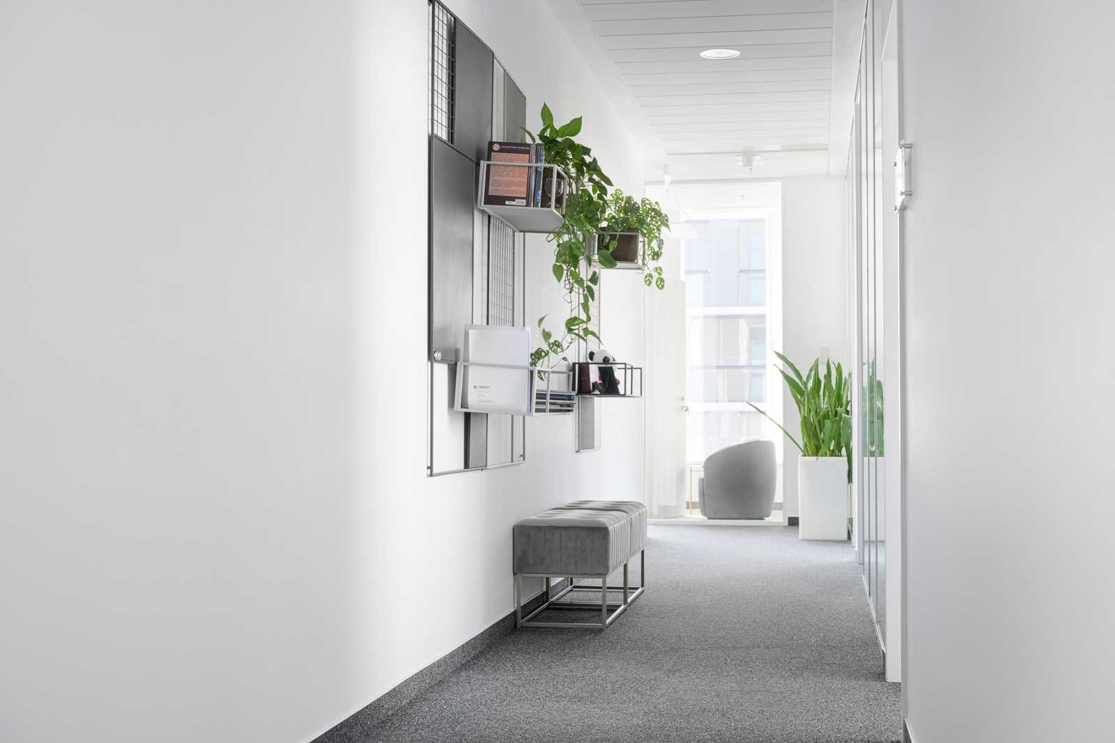Modern office hallway with plants and gray bench.