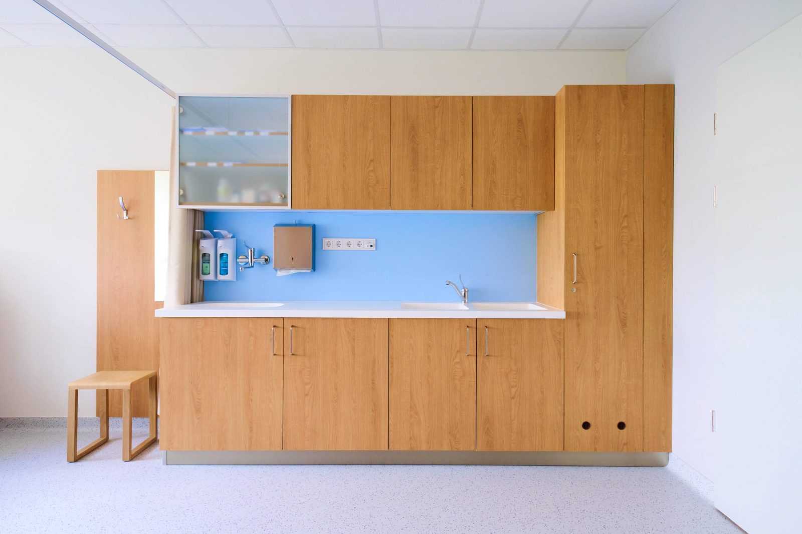 Modern wooden cabinetry in a clean medical examination room with blue backsplash.