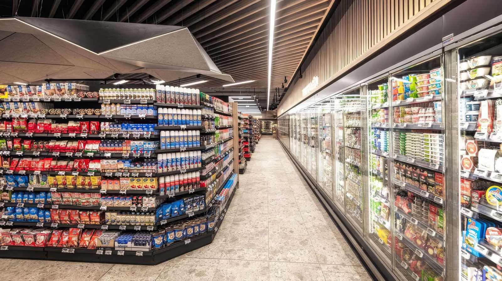 Modern supermarket aisle with refrigerated and dry goods shelves.