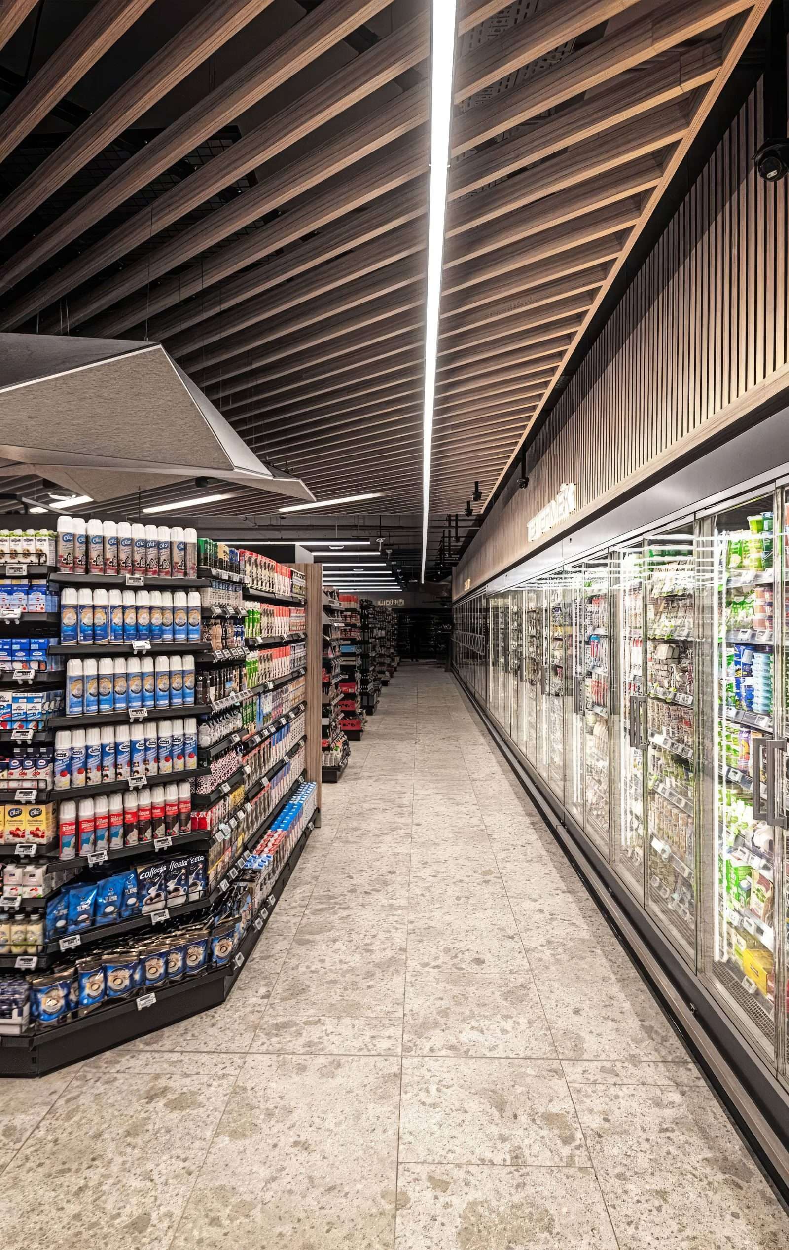 Modern supermarket aisle with wooden ceiling and refrigerated sections.