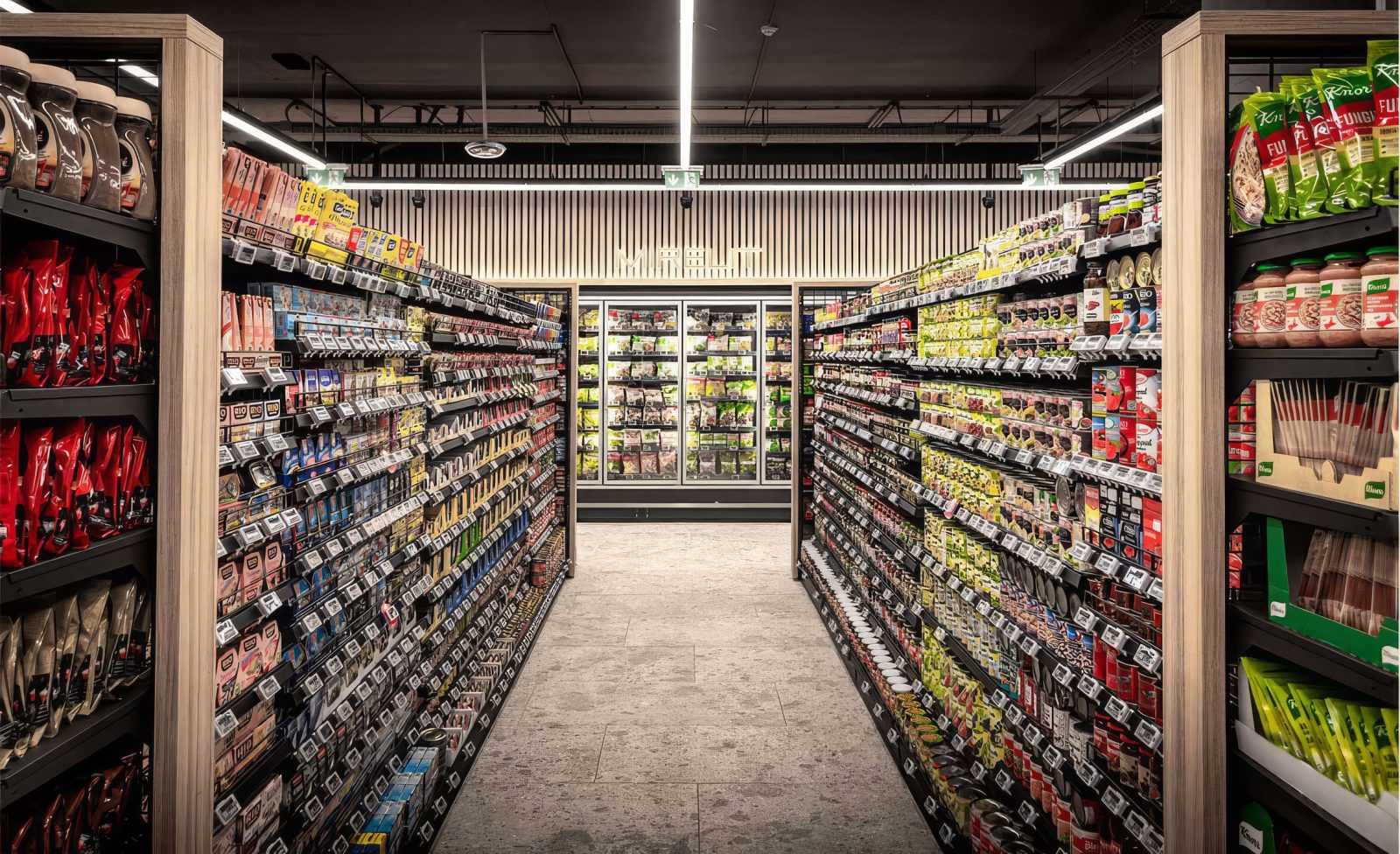 Modern supermarket aisle with well-stocked shelves and refrigerated section.