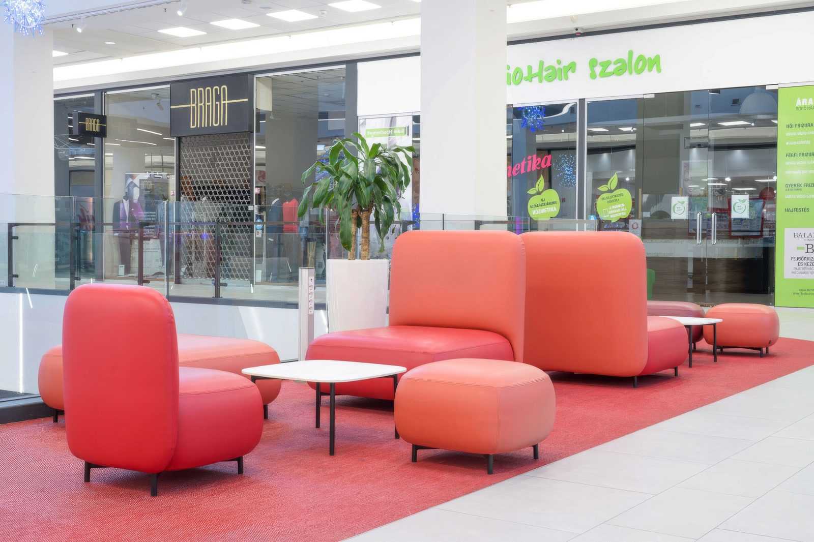 Modern red seating area in a shopping mall with stores in background.
