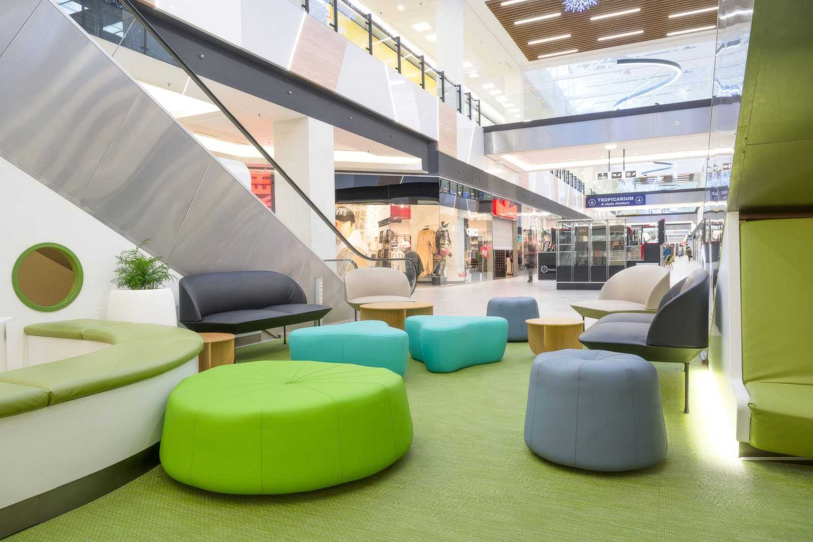 Modern shopping mall seating area with colorful furniture and escalator.