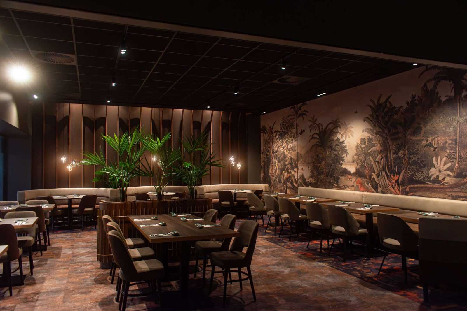 Modern restaurant interior with jungle mural and wooden tables.