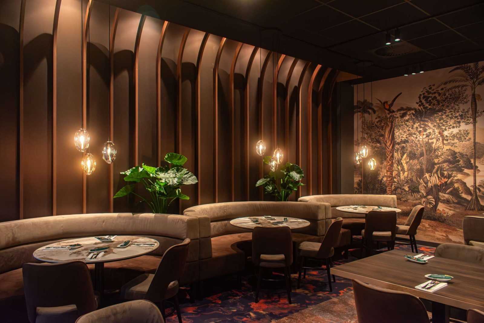 Modern restaurant interior with curved booths, hanging lights, and jungle mural.