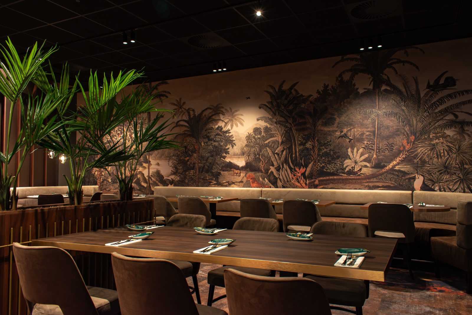 Luxury restaurant interior with jungle mural and tropical plants.