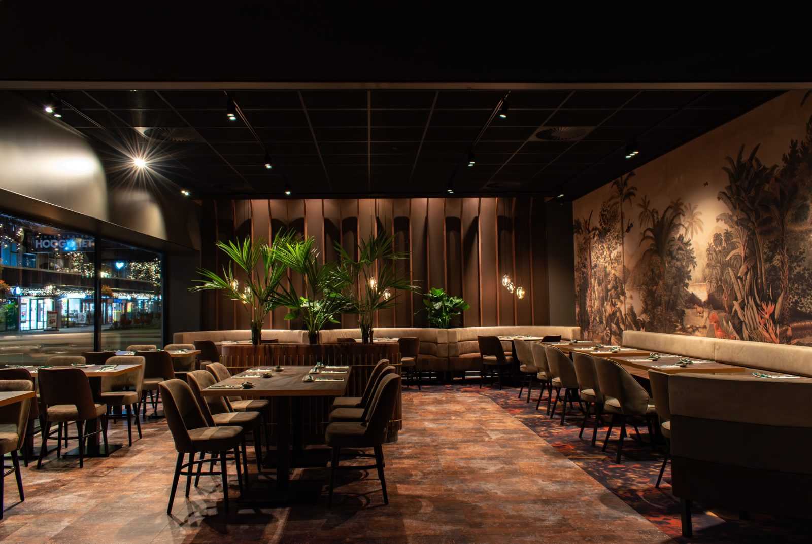Modern restaurant interior with tropical mural and wooden tables.