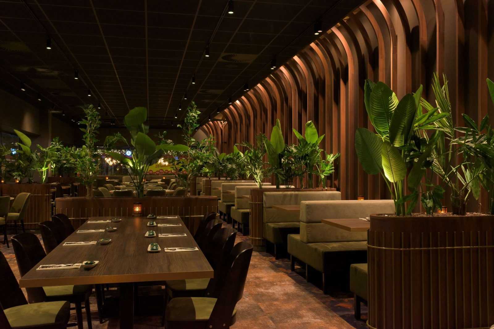 Modern restaurant interior with wooden walls and lush green plants.