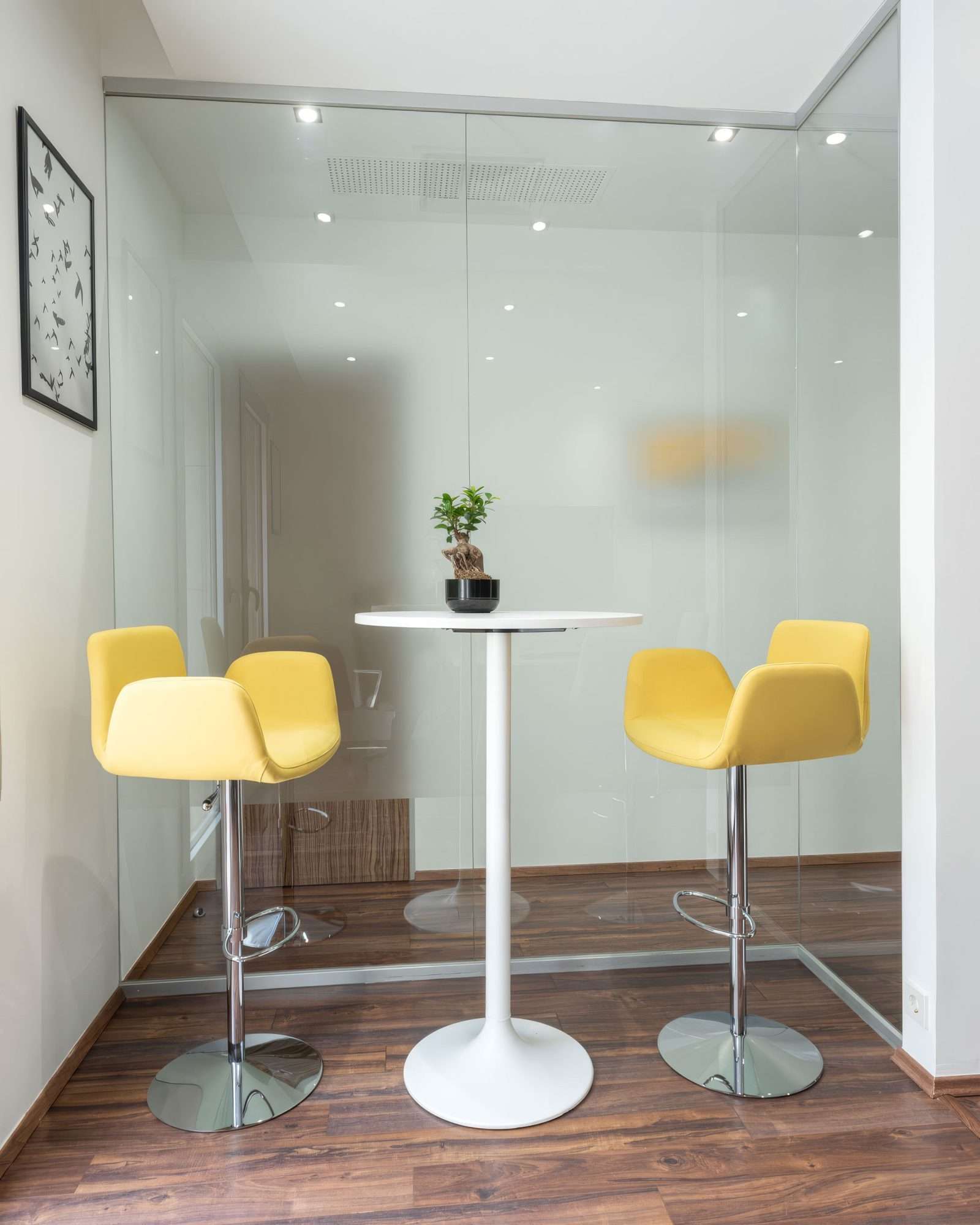 Modern office lounge with yellow bar stools and glass walls.