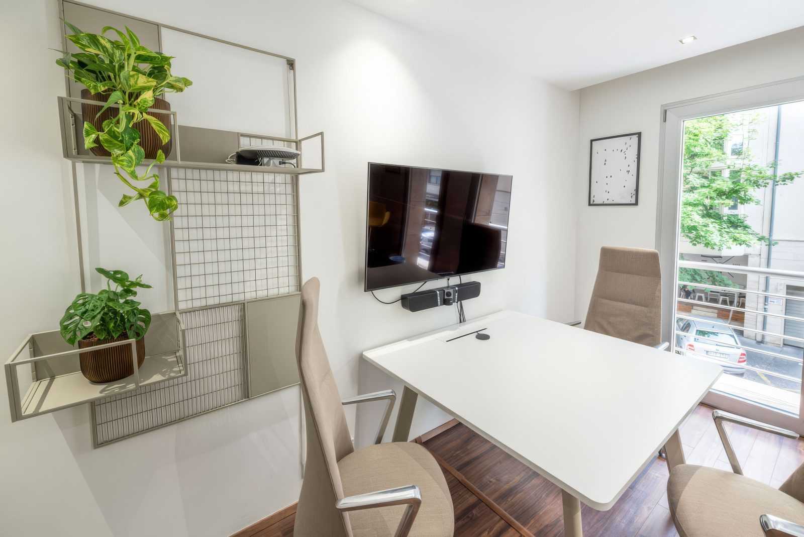 Modern office space with white desk, chairs, TV, and indoor plants.