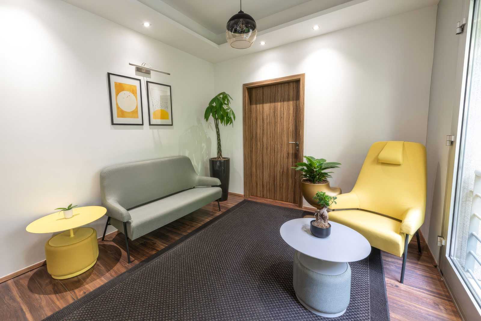 Modern living room with yellow chair, wooden door, and green sofa.
