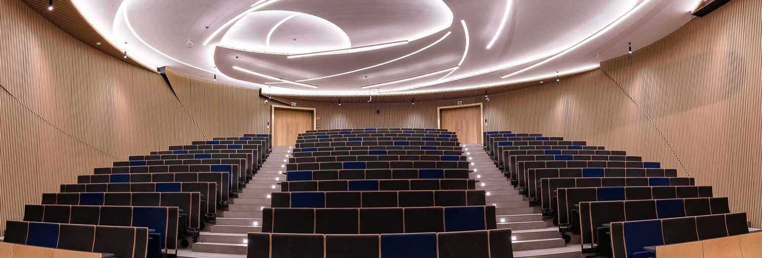 Modern wooden auditorium with tiered seating and curved ceiling lighting.