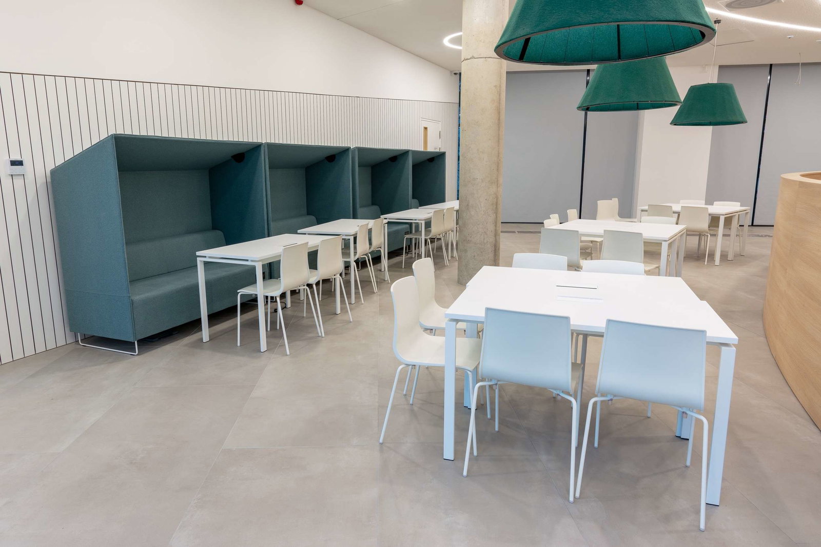 Modern office lounge with teal booths and white tables.