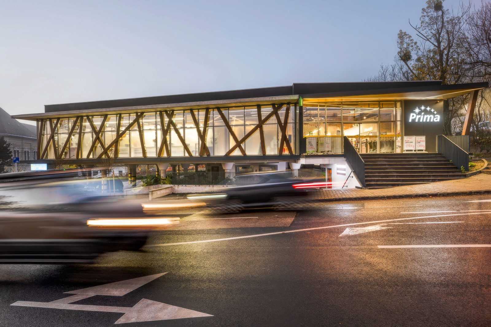 Modern Prima store with glass facade and wooden beams at dusk.