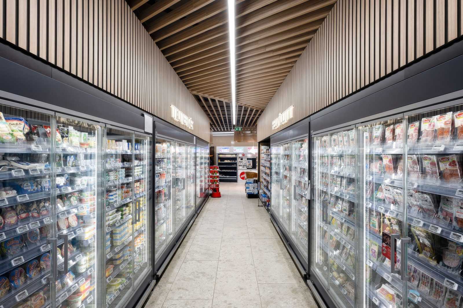 Modern supermarket refrigerated aisle with wooden ceiling and glass doors.