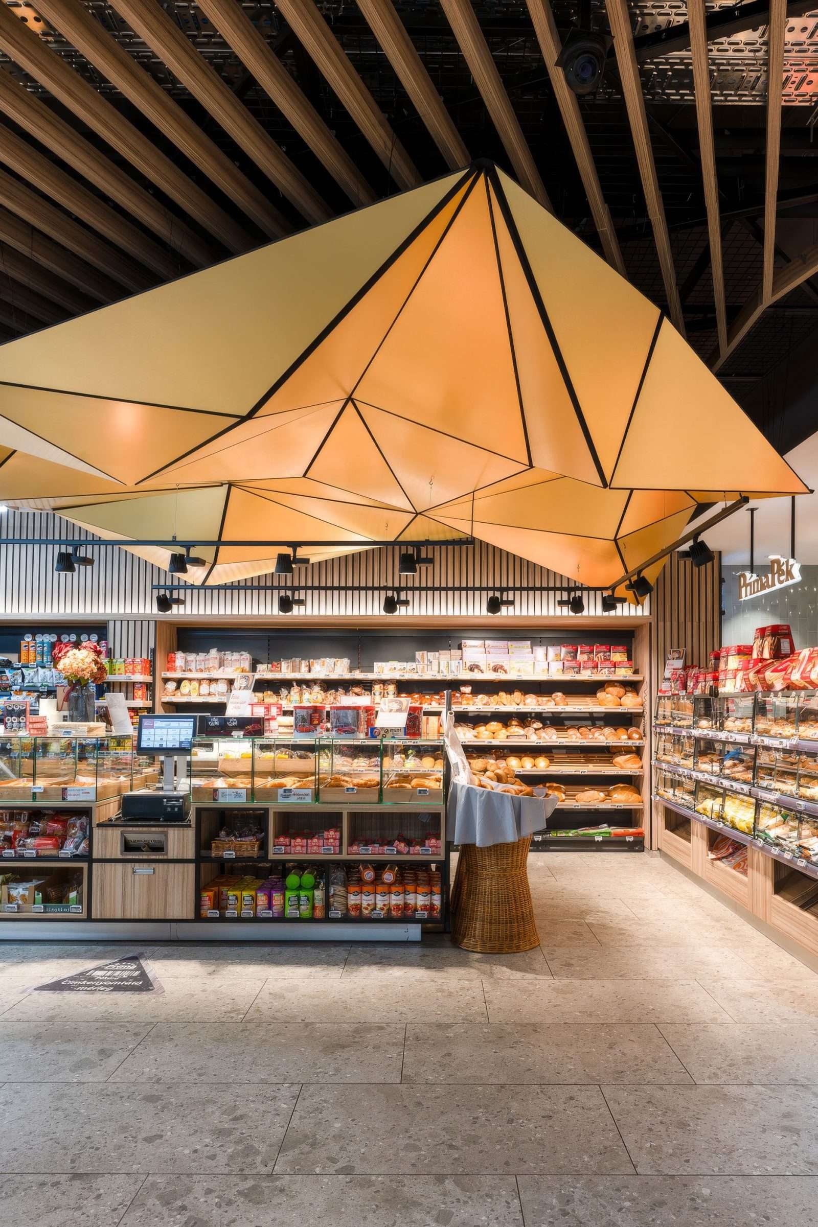 Modern bakery interior with geometric light fixture and wooden ceiling.