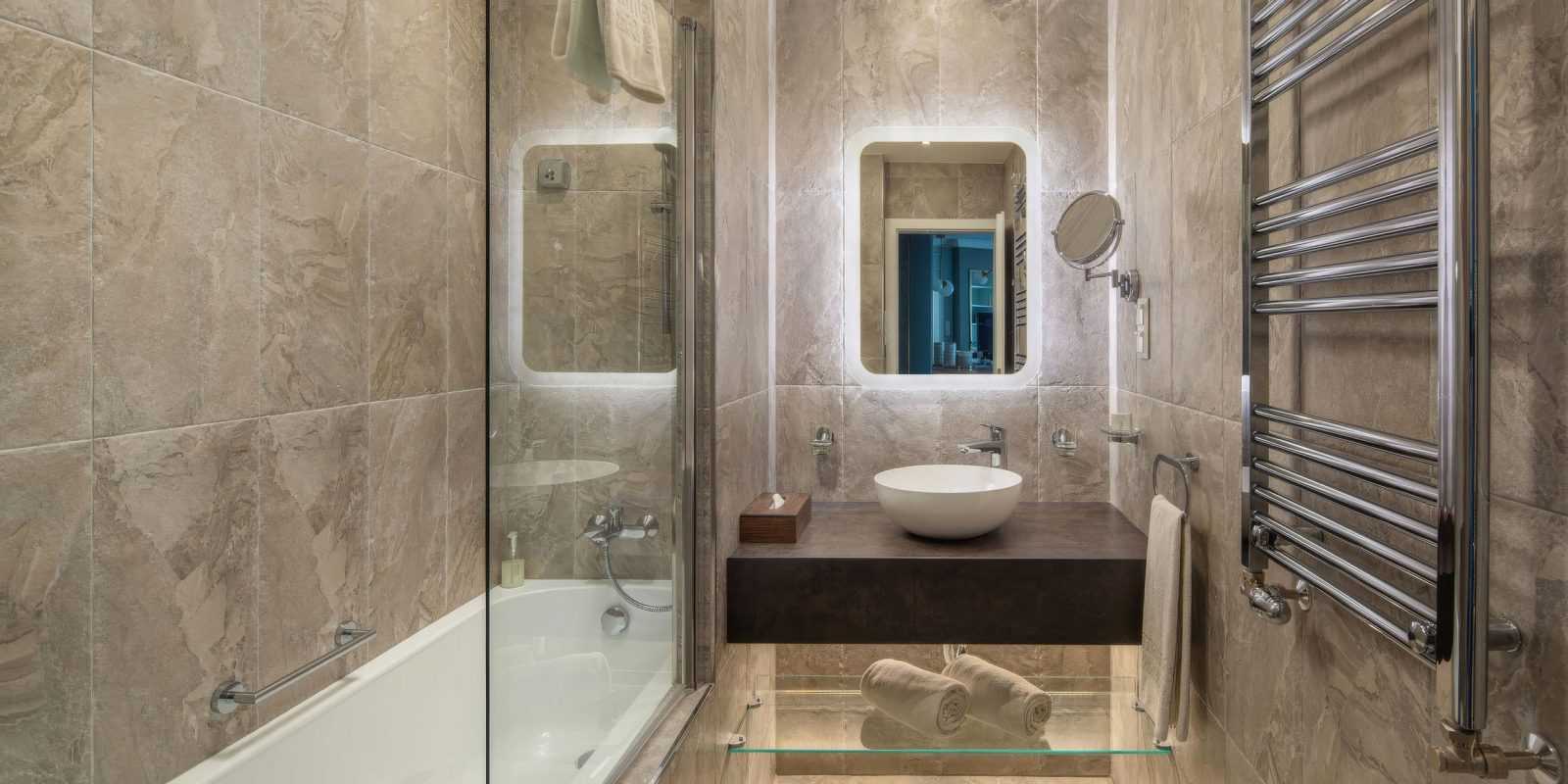 Modern bathroom with marble tiles, glass shower, and floating sink.
