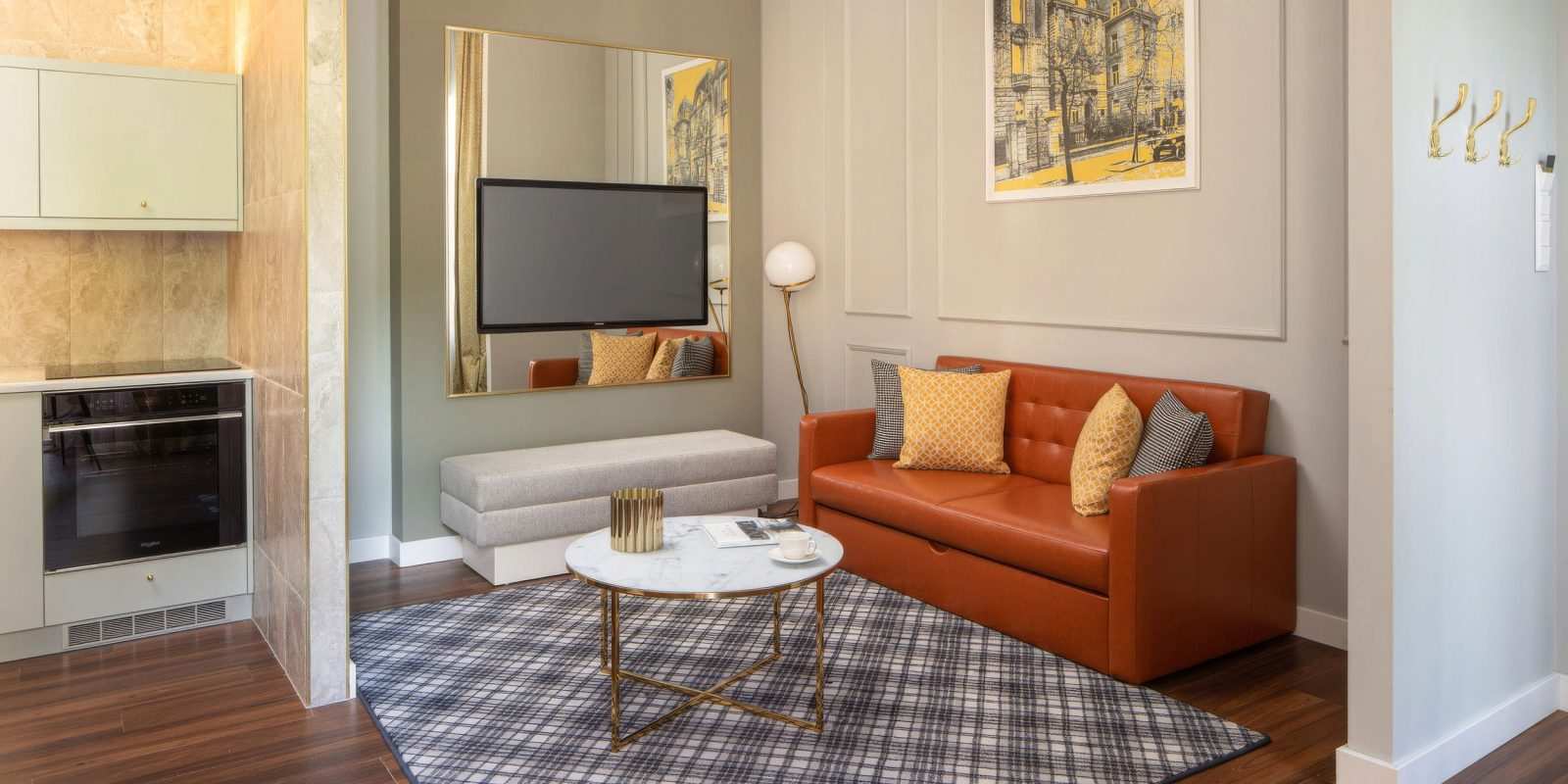 Modern hotel room with orange sofa, TV, and kitchenette.