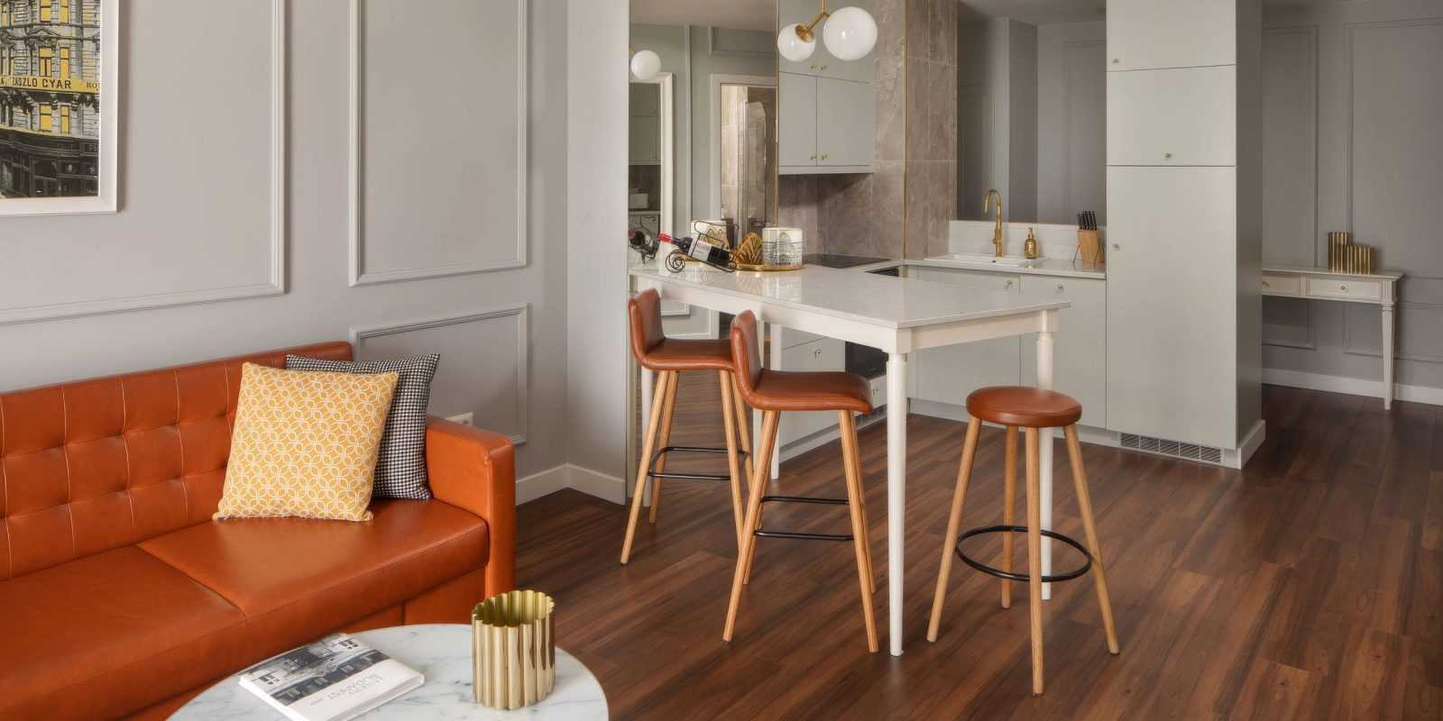 Modern apartment interior with orange sofa, kitchen bar, and wooden floors.