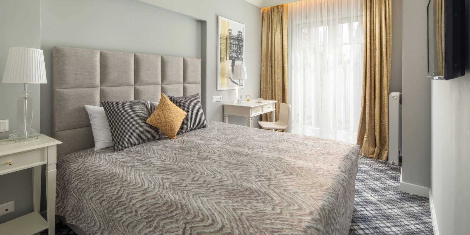 Elegant hotel bedroom with gray bed, gold curtains, and modern decor.