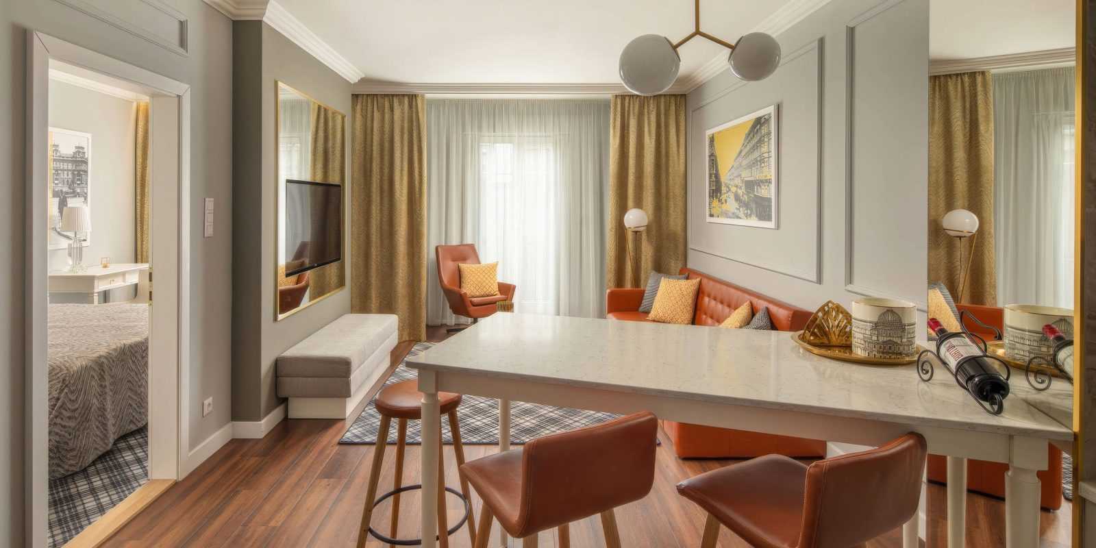 Modern hotel room with orange leather sofa, dining table, and view into bedroom.