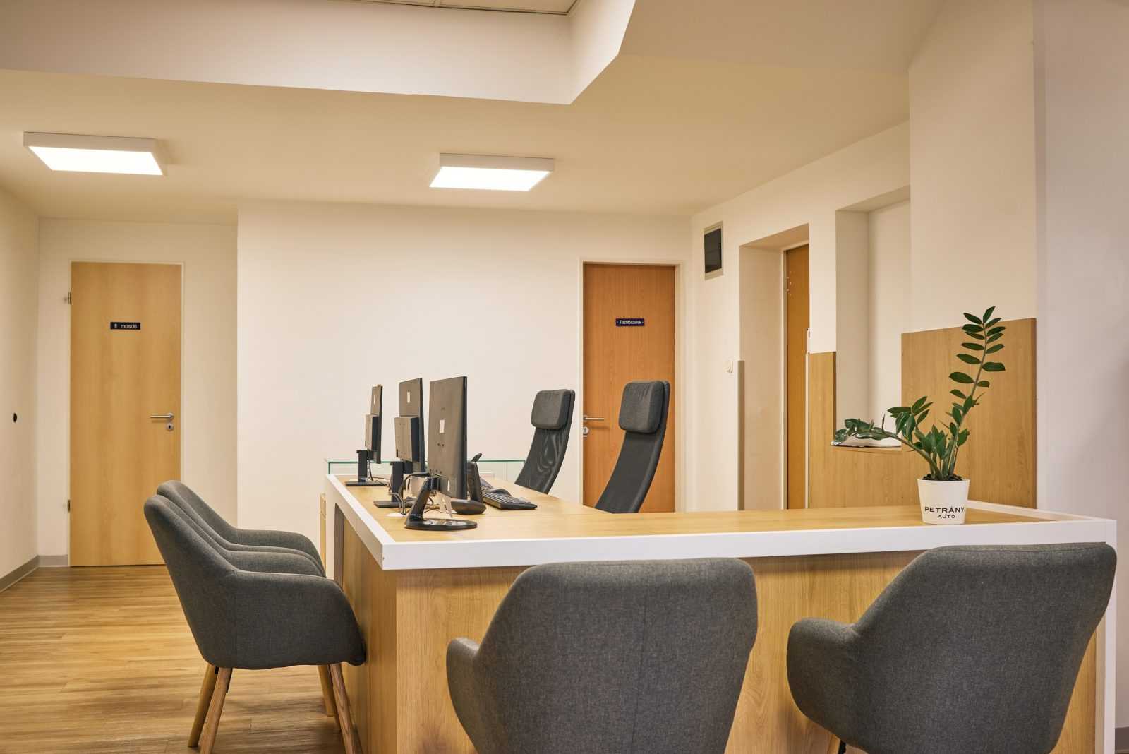 Modern office reception with wooden desk, computer stations, and gray chairs.