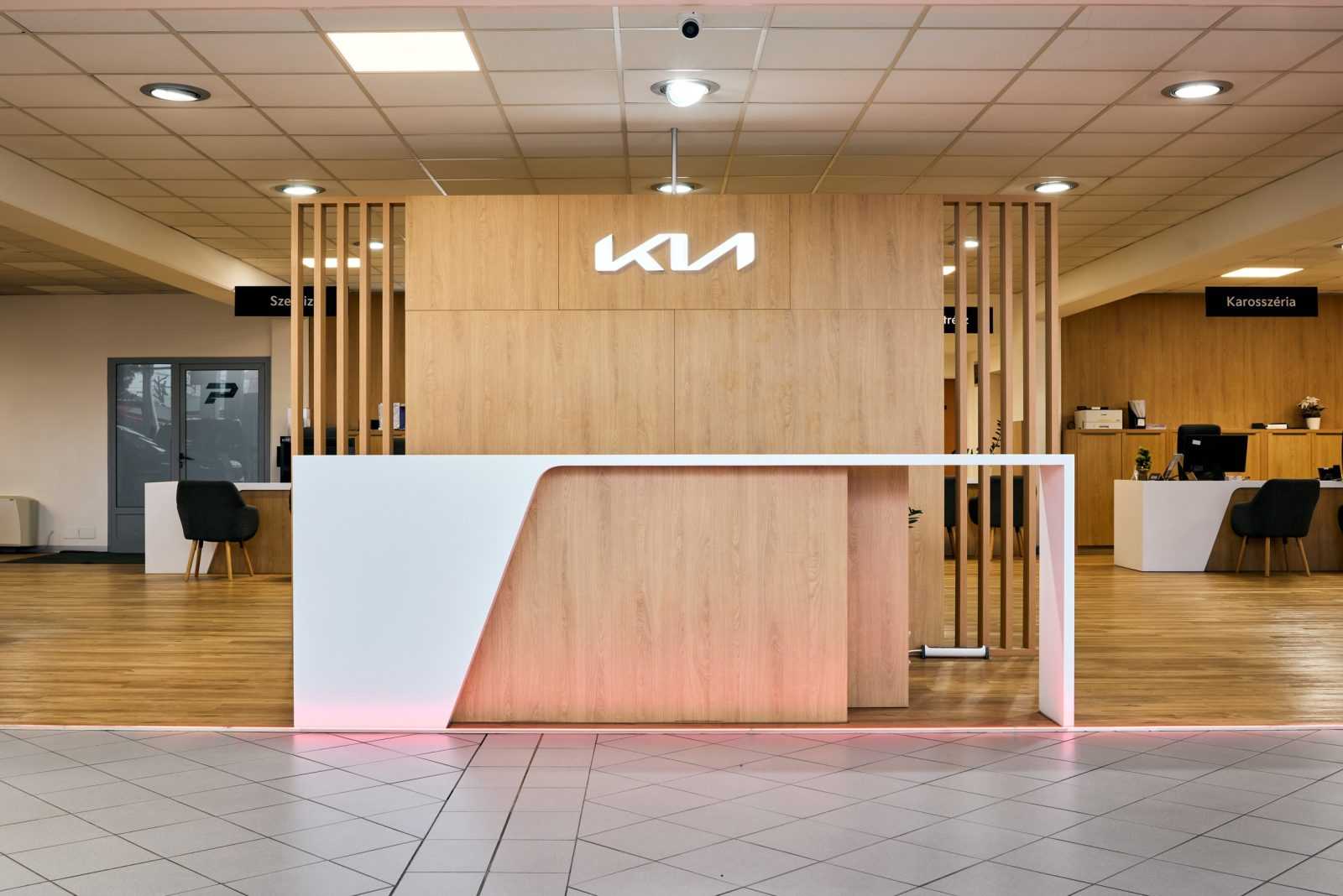 Modern Kia dealership reception with wooden design and illuminated logo.