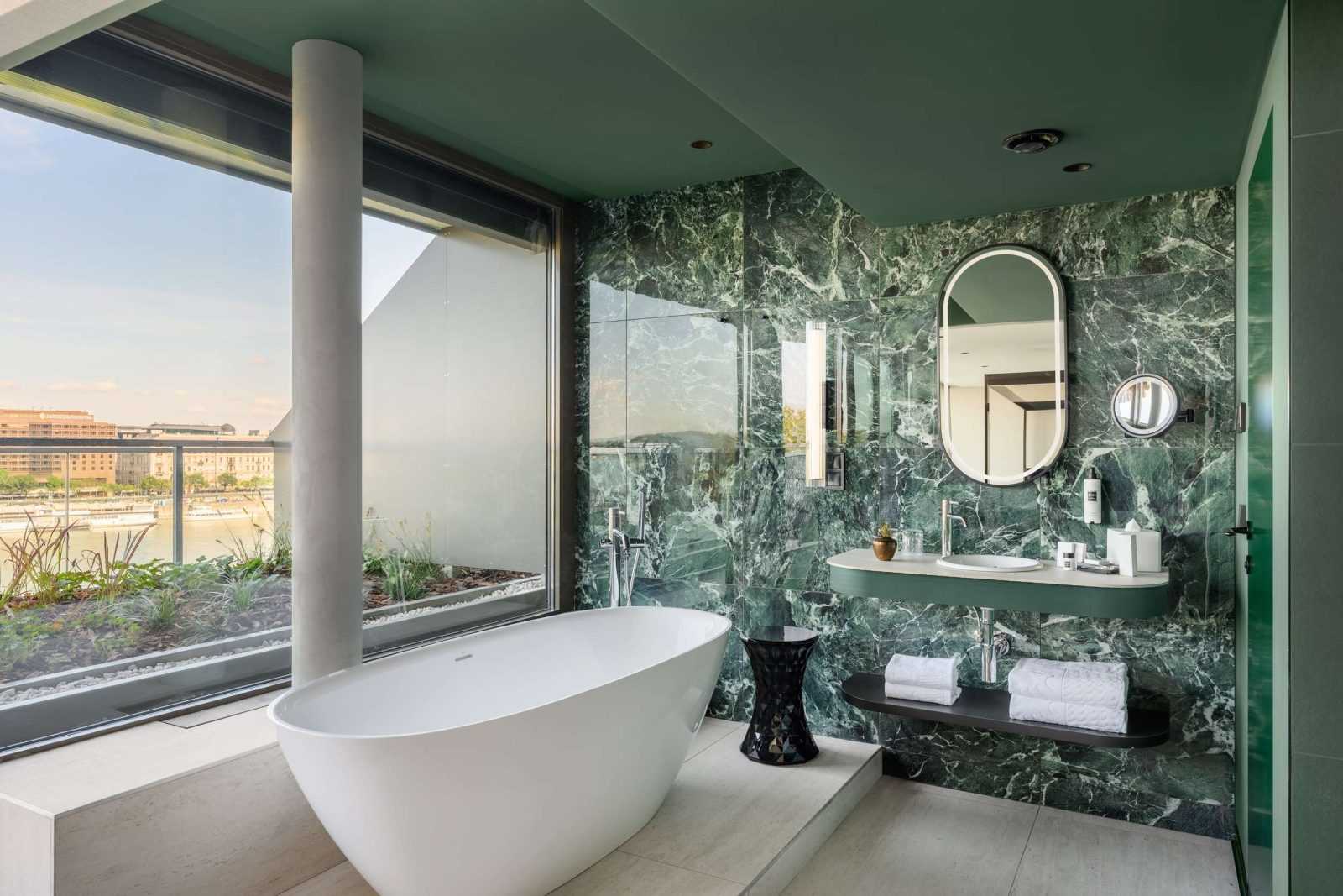 Luxury bathroom with green marble walls and bathtub overlooking river.