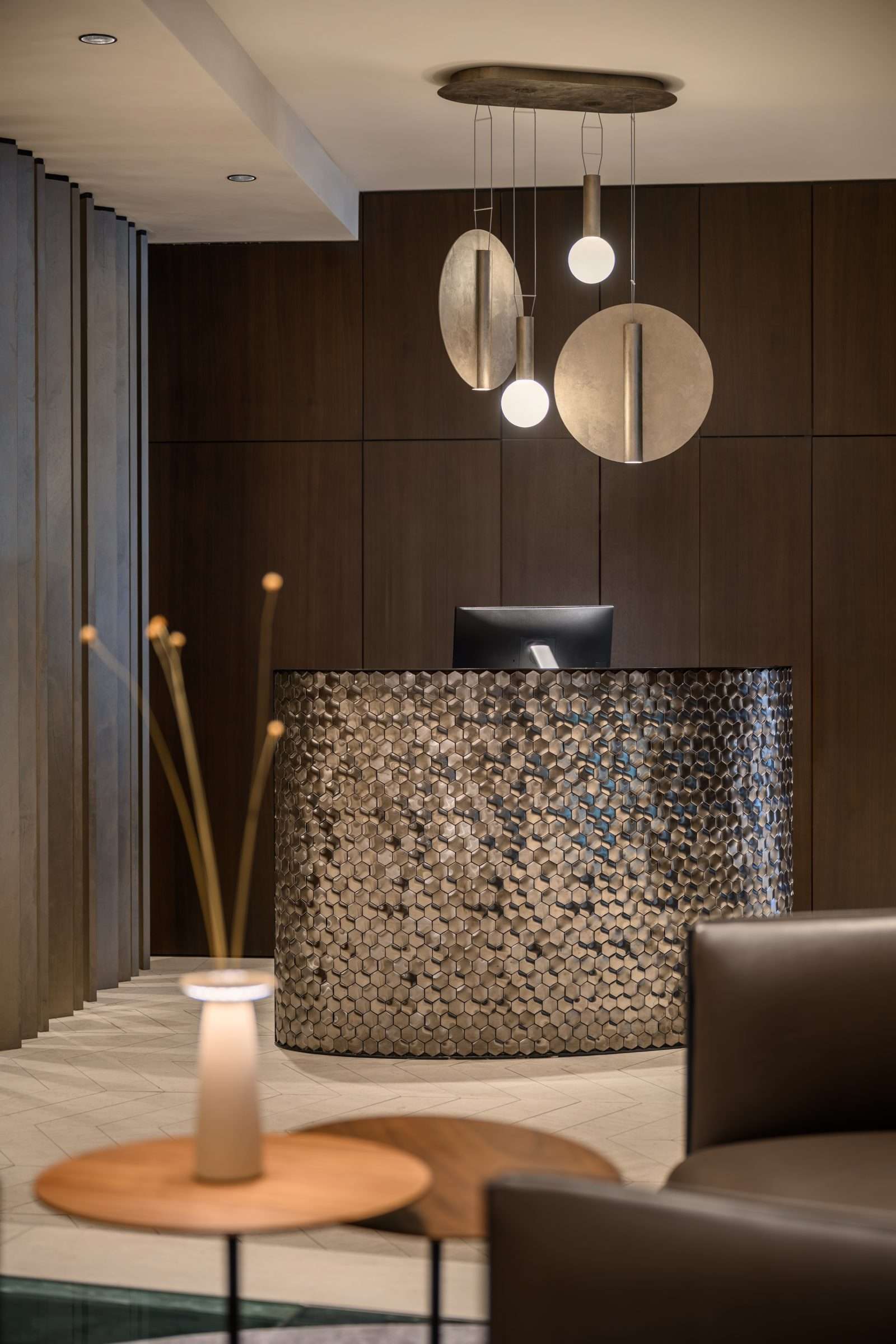Modern luxury hotel lobby with hexagonal metal reception desk and sculptural pendant lights.