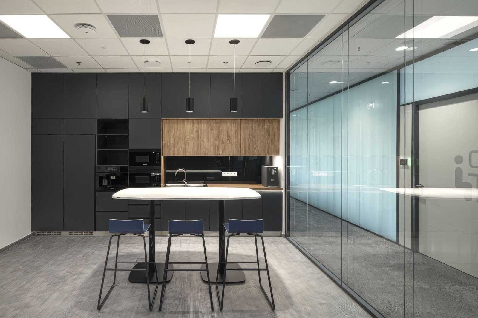 Modern office kitchen with sleek black cabinets and glass partitions.