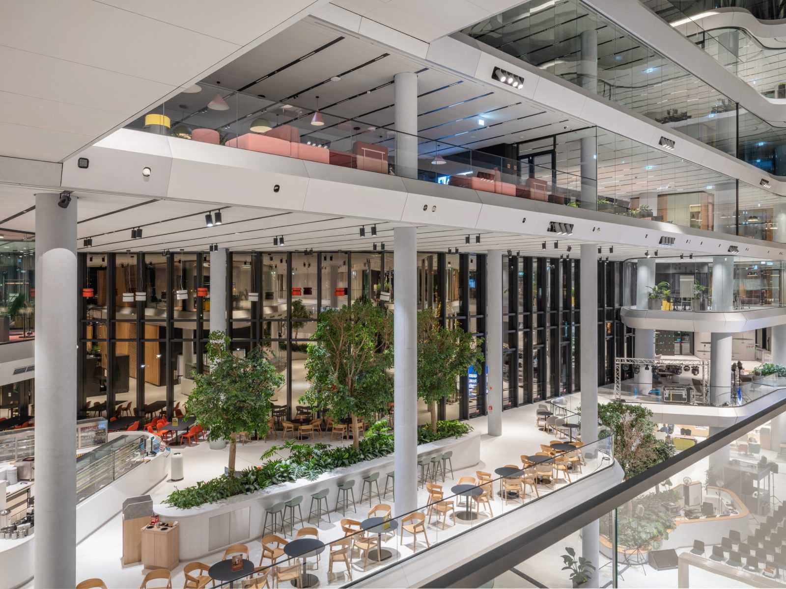 Modern multi-level office atrium with glass railings and indoor trees.