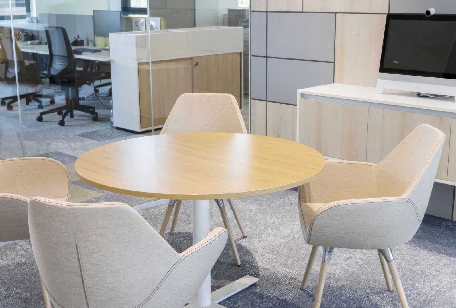 Modern wooden round table with beige chairs in a contemporary office meeting room.