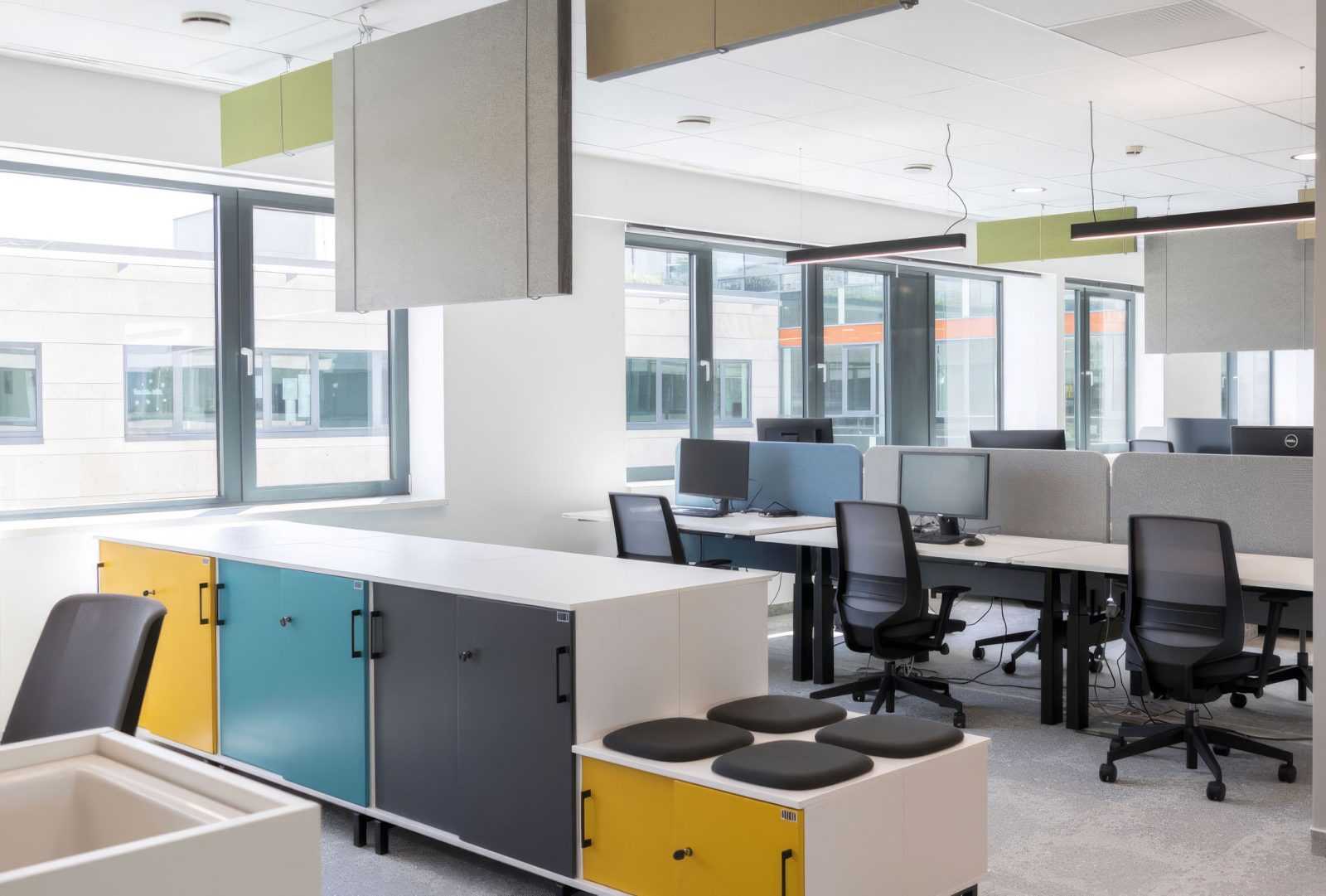 Modern office interior with colorful cabinets and ergonomic workstations.