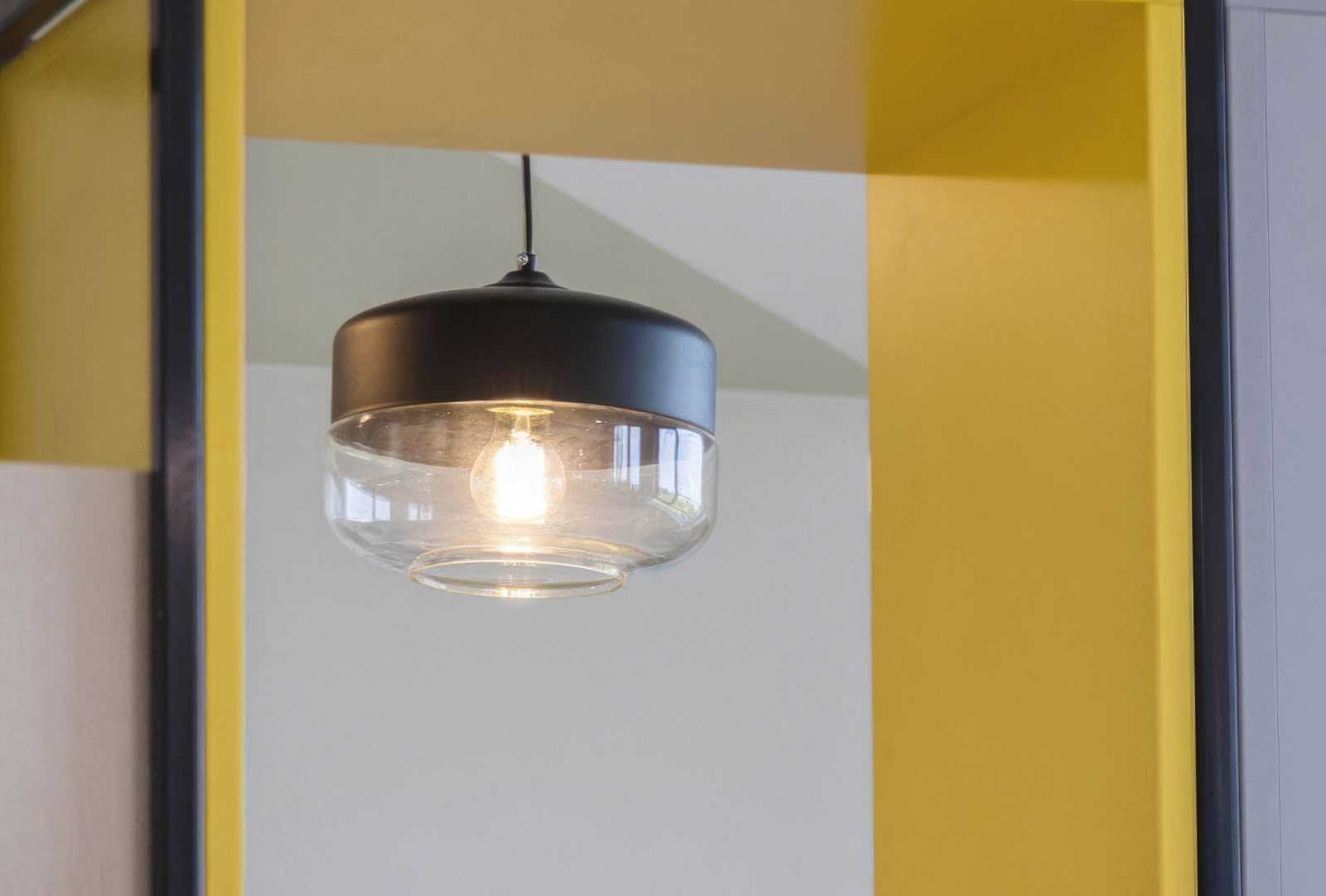 Modern pendant light with glass shade hanging in yellow and white room.