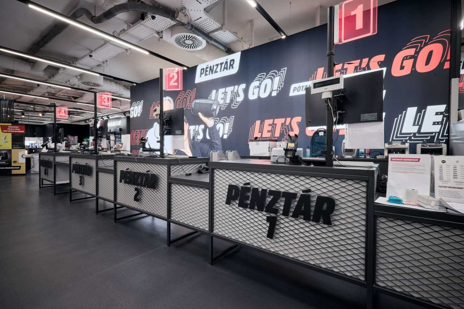 Modern checkout counters in Megaholz store with 'Pénztár' signs and 'Let's Go!' wall graphics.
