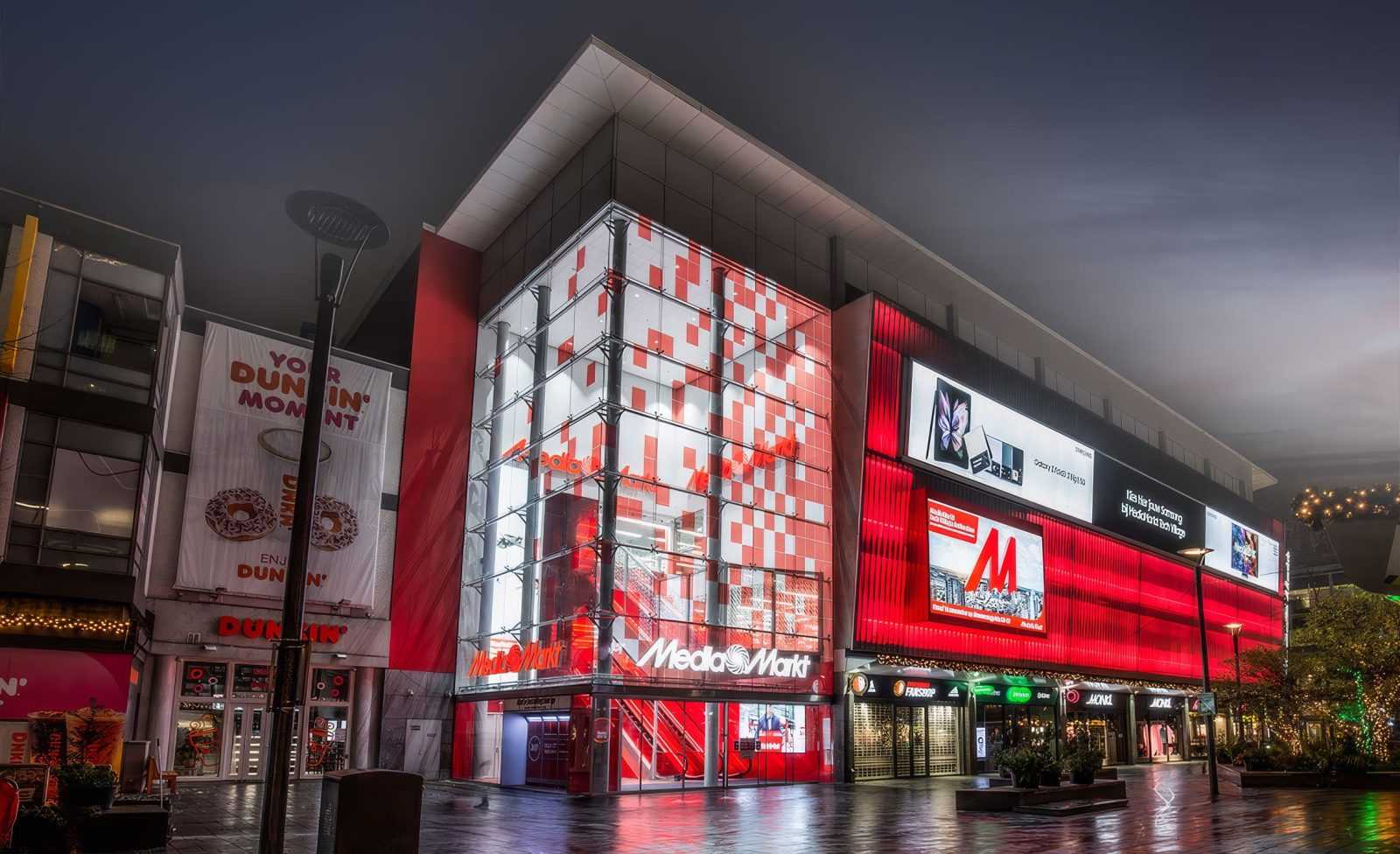MediaMarkt store at night with red lighting and Dunkin' Donuts adjacent.