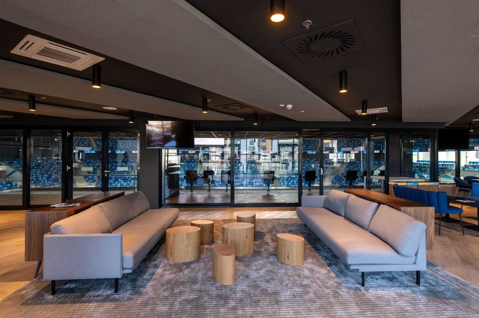 Modern lounge area at Megaholz with sofas and wooden tables overlooking stadium seating.