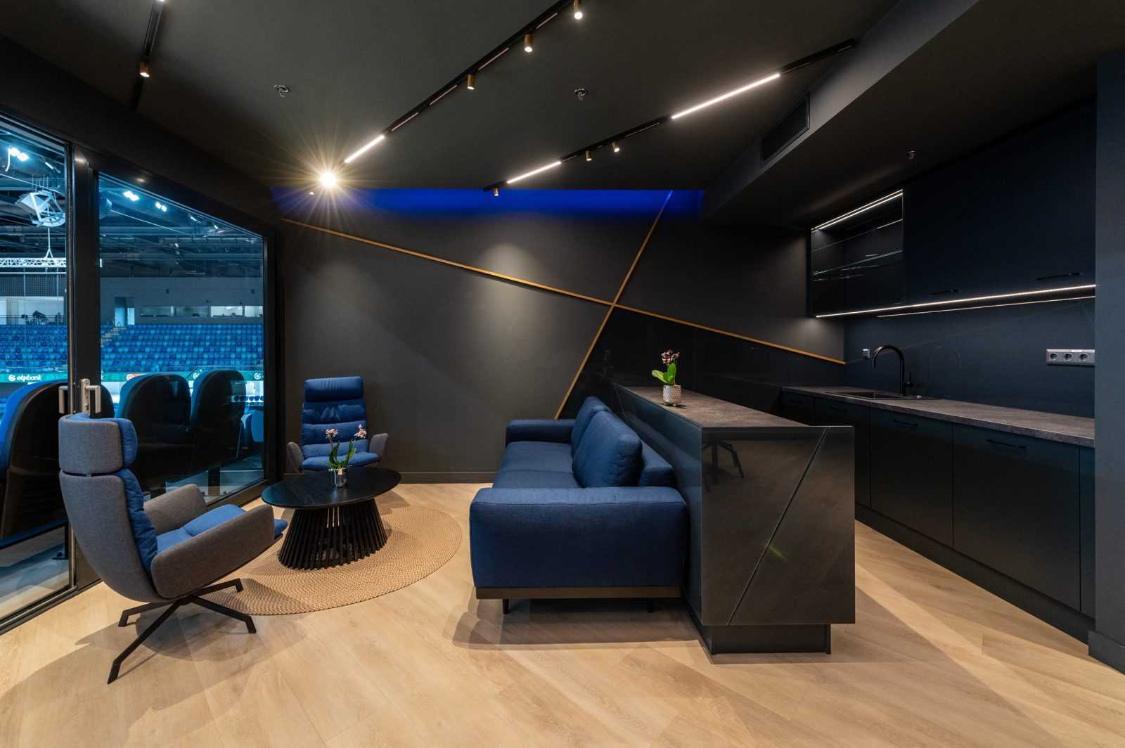 Modern luxury lounge with blue sofas and sleek kitchen in stadium suite.