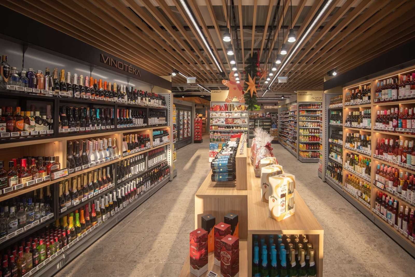 Modern wine and spirits store aisle with wooden ceiling and festive decorations.