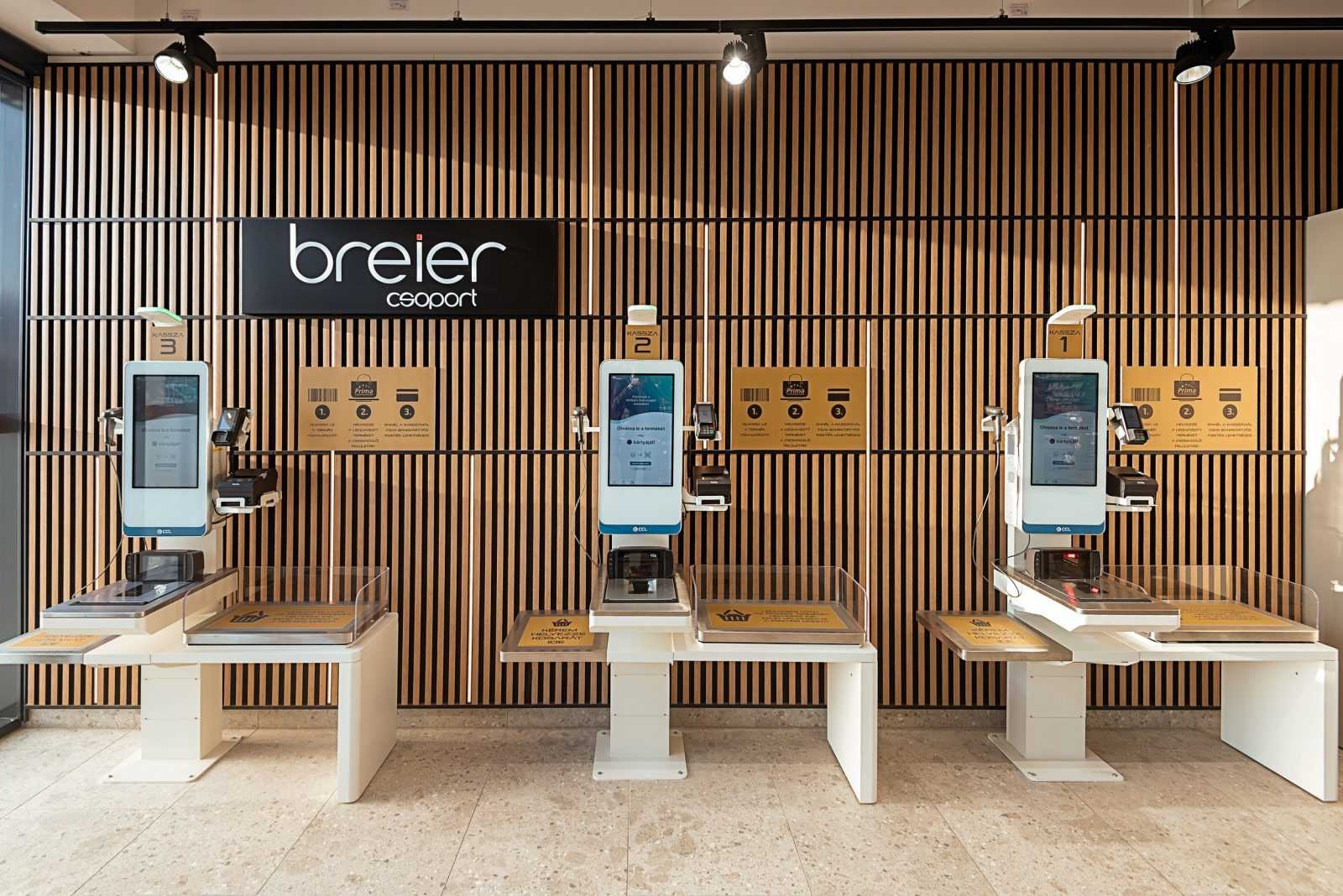 Modern self-checkout kiosks at Breier Csoportház with wooden wall design.