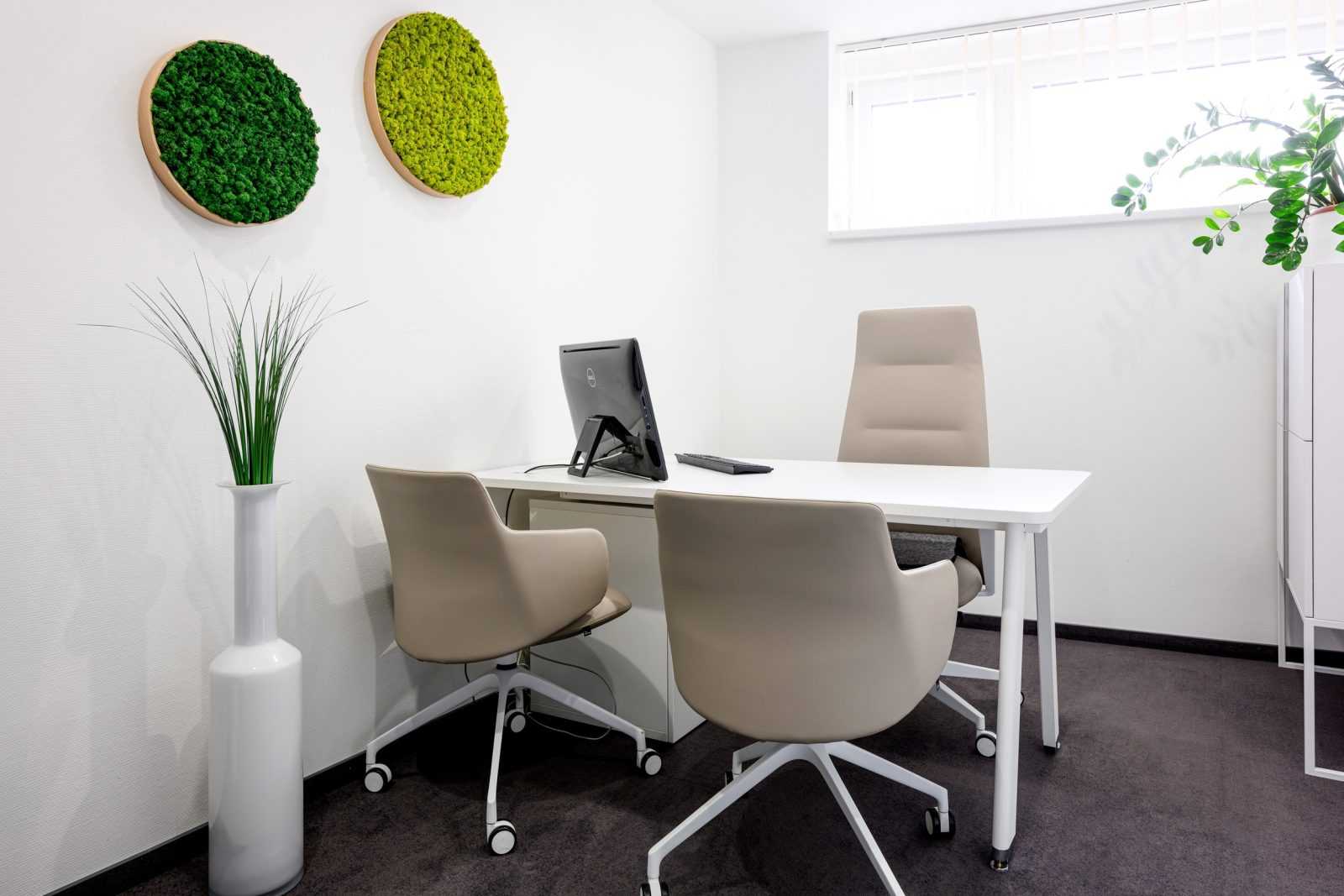 Modern office space with white desk, beige chairs, and green wall decor.