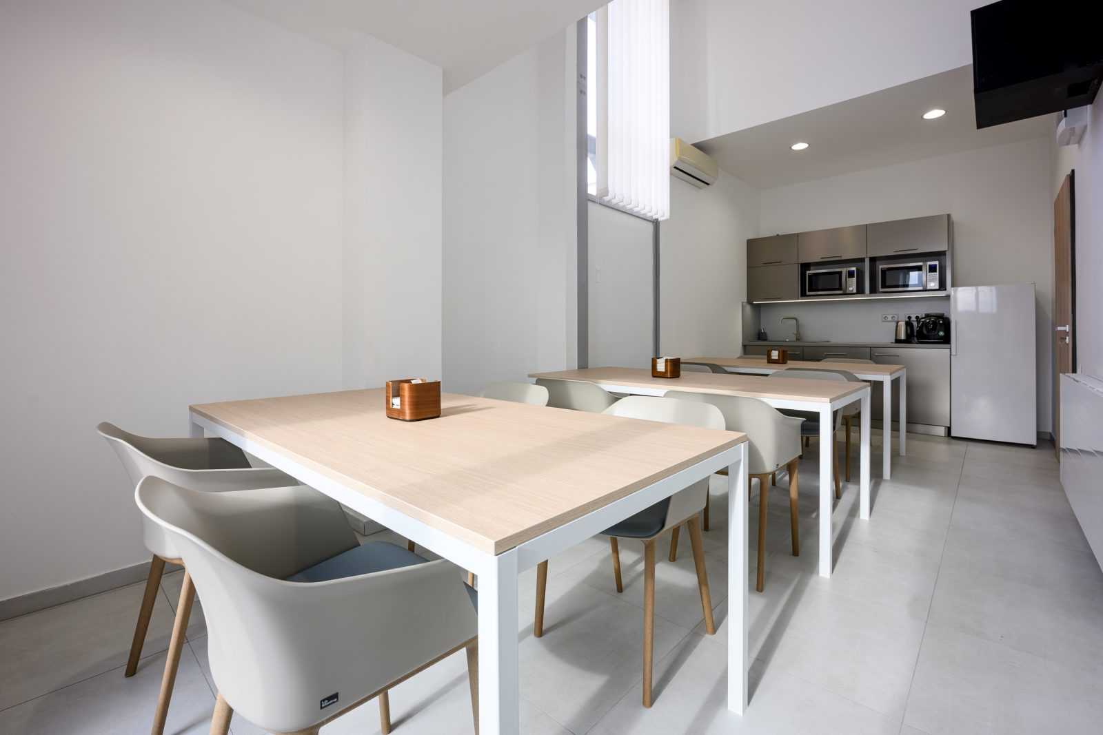 Modern minimalist dining area with wooden tables and chairs in a clean apartment kitchen.